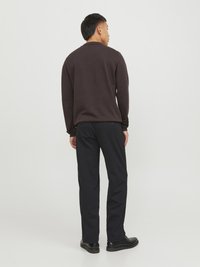 Camicia marrone scuro a maniche lunghe e pantaloni neri. La camicia ha un design semplice; i pantaloni sono dritti e hanno una texture liscia. Le scarpe nere completano il look.