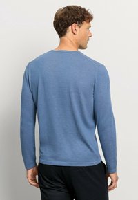 Langärmliges Hemd aus leicht blauer Baumwolle, mit einem klassischen Rundhalsausschnitt und einer lockeren Passform; getragen mit dunklen Hosen.