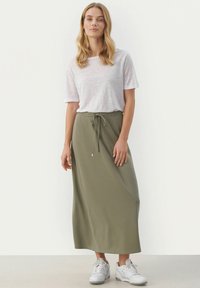 Lys grå kortærmet T-shirt med rund hals, stoppet ned i en olivengrøn ankel-lang nederdel med snoretræk i taljen, sammen med hvide sneakers.