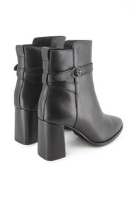 Botas de cuero negras hasta el tobillo con punta afilada, tacón apilado y hebilla decorativa en el costado. Textura suave, diseño minimalista.