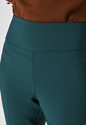Pantaloni teal a vita alta realizzati in tessuto liscio, con una cintura morbida e cuciture pulite, progettati per un look aderente.