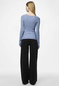 Gofruotas, ilgomis rankovėmis megztinis šviesiai mėlynos spalvos, derinamas su plačiomis juodomis kelnėmis. Sukurtas su apvaliu iškirpimu nugaroje ir prigludusia siluetu.