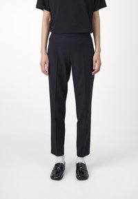 Tailored dark navy dress pants with front pleats, smooth texture, slim fit, and side pockets, paired with black loafers and white socks.