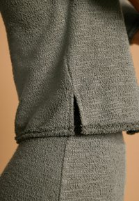 Szary strój z tkaniny frotte o teksturowanej powierzchni, z rozcięciem na dole topu i dopasowanym dołem. Prosty fason bez wzorów.