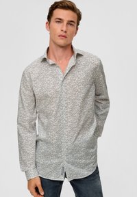 Langarmshirt aus leichtem Stoff mit geometrischem Druck in Blau. Klassischer Kragen, durchgehende Knopfleiste und abgerundeter Saum. Getragen mit dunklen Jeans.