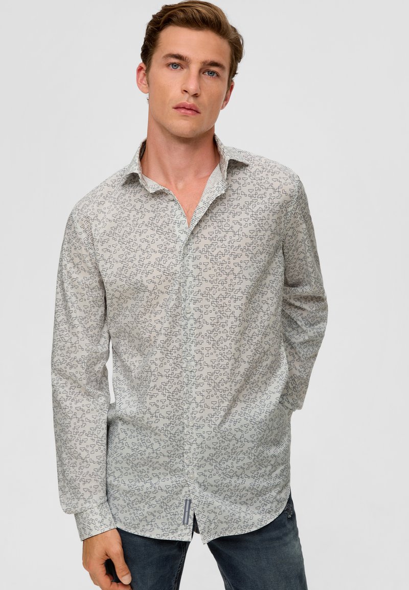 Langarmshirt aus leichtem Stoff mit geometrischem Druck in Blau. Klassischer Kragen, durchgehende Knopfleiste und abgerundeter Saum. Getragen mit dunklen Jeans.