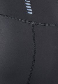 Leggings sportivi neri con una texture liscia, cuciture a contrasto e strisce riflettenti minimaliste sulla vita per una maggiore visibilità.