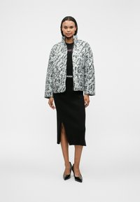 Καπιτονέ μπουφάν με μοτίβο μαύρου και λευκού χρώματος, διαθέτει ψηλό γιακά και μπροστινές τσέπες, συνδυασμένο με εφαρμοστό μαύρο ριμπ φούστα.