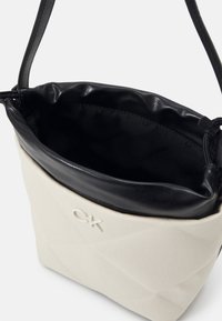 Petit sac à épaule Calvin Klein beige et noir avec extérieur en tissu matelassé et doublure intérieure noire lisse.
