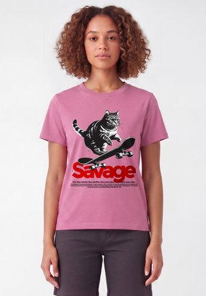 Frau trägt ein pinkes Hemd mit einer schwarz-weißen Katze, die Skateboard fährt, über fettem rotem "Savage" Text und kleinerem motivierendem Text darunter.