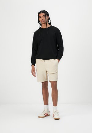 Black sweatshirt with long sleeves, beige corduroy shorts, and beige sneakers with red accents. Simple design, relaxed fit.
