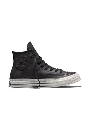 Zapatilla deportiva negra alta de piel con suela de goma blanca y cordones negros, mostrando perfil lateral con parche visible del logo de la marca.