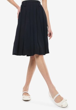 Marineblauwe plissé rok met een fitted taille en een flared silhouet, gecombineerd met witte leren ballerina's met een strikaccent en een bandje.