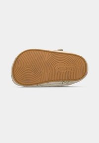 Παντόφλα με λουλουδάτο σχέδιο, λευκό επάνω μέρος και υφή μπεζ ελαστικής σόλας. Η σόλα διαθέτει διακριτικό κυματιστό σχέδιο για πρόσφυση.