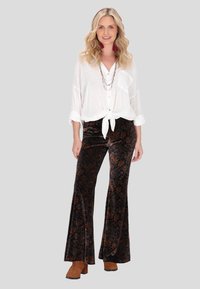 Blusa bianca con bottoni e fronte annodato. Pantaloni flared in velluto scuro a fantasia floreale paisley. Stivaletti marroni alla caviglia. Collane a più strati.