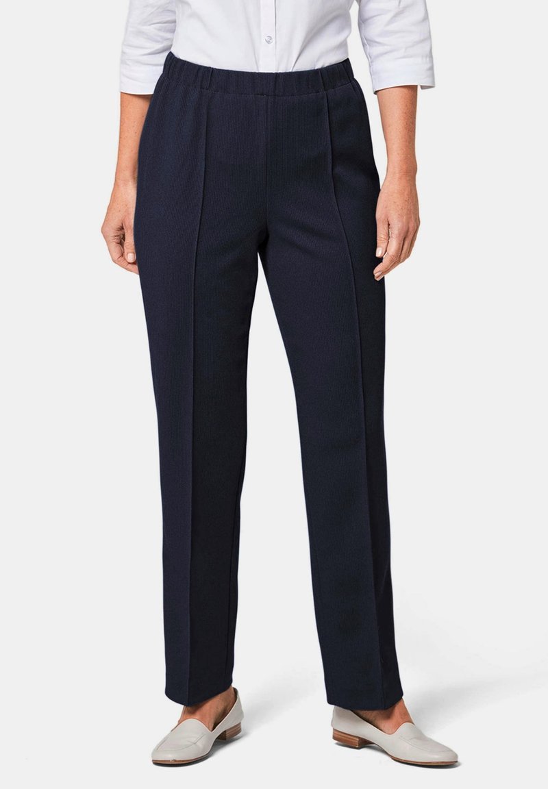 Navyblauwe, rekbare stoffenbroek met een tailleband; beschikt over verticale naden voor een gekleed uiterlijk, gecombineerd met lichte schoenen.