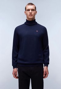 Navy blue turtleneck sweater with ribbed cuffs and hem, featuring a small red and white logo on the left chest. Soft, knitted fabric.