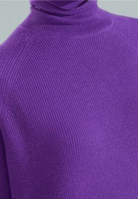 Lähikuva purppurasta ribbikuvioidusta kaulustakista, joka näyttää tekstuuria ja ompeluyksityiskohtia olkapäillä ja kauluksessa.