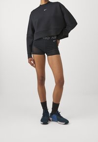 Felpa nera corta con maniche lunghe, abbinata a pantaloni sportivi neri con una vita con logo. Modello che indossa scarpe da ginnastica blu navy con calze nere.