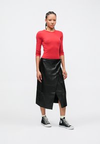 Punane pika varrukaga top, mida on kombineeritud musta nahast midi seelikuga, millel on diagonaalsed õmblused ja esihõlmadega lõhik, kantud mustade kõrgete tennistega.