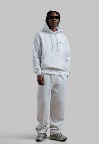 Felpa grigia chiara con tasca frontale, cappuccio regolabile e testo blu "POCKETS". Abbinata a pantaloni della tuta grigi coordinati e sneakers grigie.