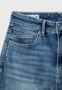 Gros plan d'une poche de jean en denim bleu avec une boucle de ceinture visible, des rivets métalliques et une étiquette de taille indiquant le numéro 36.