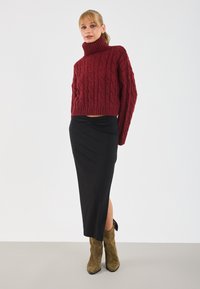 Maglione a collo alto lavorato a maglia spesso di colore rosso, con design corto. Gonna midi aderente nera con spacco laterale. Stivali alla caviglia verde oliva con finitura texturizzata.