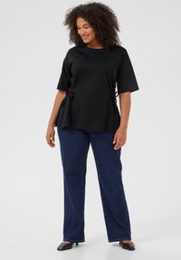 Top negro con mangas cortas y lazos laterales, combinado con jeans de mezclilla azul oscuro. La tela parece suave con un ajuste relajado.