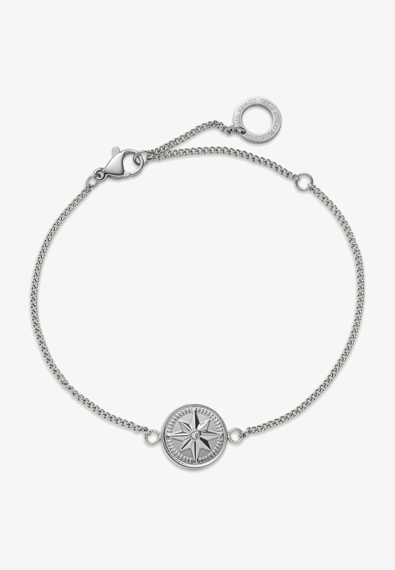 Silver chain bracelet with a round compass rose charm in the center and a circular tag near the clasp engraved with text.