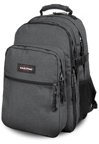Mochila gris con una tela texturizada, que cuenta con múltiples compartimentos con cremallera y un bolsillo lateral de malla. Incluye un asa superior y correas ajustables.