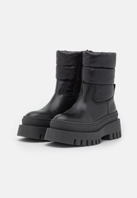 Schwarze Knöchelschuhe mit einem glatten Lederuntergrund und gepolstertem, gestepptem Obermaterial. Dicke Plattformsohle mit geriffelter Struktur für besseren Halt.