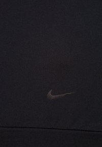 Sort atletisk stof med et subtilt Nike swoosh-logo i en mørkere nuance, der fremhæver tekstur og enkelhed i designet.