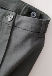 Pantalon en tissu gris présentant une texture lisse, une fermeture à bouton avec un design à quatre trous, et des passants pour ceinture.