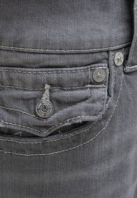 Jeans de mezclilla gris con un bolsillo trasero con costura visible, botones de hardware plateado y un acento de botón de marca.