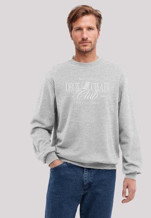 Gray sweatshirt featuring "Deck Chair Club" graphic in white lettering. Crew neck, long sleeves, and ribbed cuffs. Worn with blue jeans.