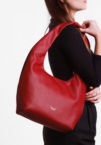 Red leather hobo bag with a soft, smooth texture, a rounded shape, and a prominent logo. Worn over the shoulder, showcasing a spacious design.