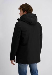 Zwarte waterdichte jas met een grote capuchon, voorzien van een minimalistisch ontwerp, warme voering en verstelbare manchetten, afgebeeld vanuit de achterkant.