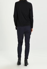 Svart långärmad skjorta kombinerad med marinblå randiga byxor, med en smal passform och elastiska ärmslut, fulländad med ankelboots.