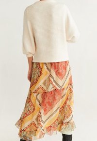 Pull en crème à la texture douce avec des manches bouffantes, associé à une jupe midi imprimée dans des tons d'orange, beige et jaune, avec des volants superposés au niveau de l'ourlet.