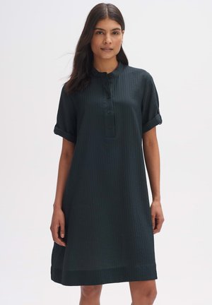 Dunkelgrünes, kurzärmliges Kleid mit knöpfbarem Einsatz, gerippter Textur, rundem Kragen und umgeschlagenen Ärmeln, das oberhalb des Knies endet.