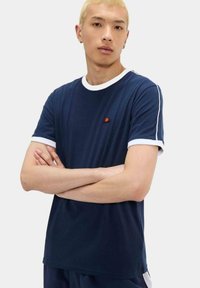 Camiseta azul marino con ribete blanco en las mangas y el cuello. Presenta un pequeño logo en el pecho. Tejido suave, corte relajado, mangas cortas.