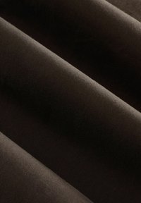 Tessuto marrone scuro con una superficie a coste, che mostra strati piegati. Il materiale appare morbido e ha una leggera lucentezza in alcune aree.