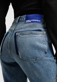 Modre kavbojke z visokim pasom, s kožnim oznako "KARL LAGERFELD JEANS" in kontrastnimi temnimi žepi.