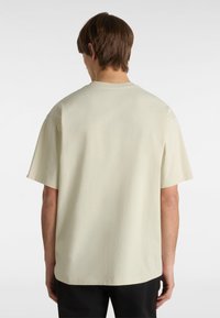 T-shirt a maniche corte di colore crema con una vestibilità rilassata, scollatura rotonda e una superficie in cotone liscia, priva di motivi o decorazioni visibili.