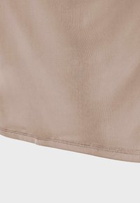 Tissu beige avec une fine couture visible le long de l'ourlet incurvé sur un fond clair.