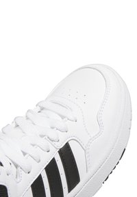 Białe sneakersy z gładką skórzaną cholewką, czarnymi paskami i płaskimi białymi sznurowadłami. Teksturowana gumowa podeszwa z perforacjami na przodzie.