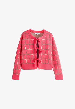 Vaaleanpunainen neuletakki neliskulmaisella kuviolla, koristeltu hopeisilla niiteillä. Pyöreä pääntie ja edestä sidottavat nauhat. Resorit hihansuissa ja helmassa.