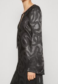 Svart klänning med ett ormmönster i varierande nyanser av grått. Har långärmar, V-ringning och dragsko vid halsringningen.