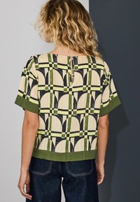 Lühikeste varrukatega top geomeetrilise mustriga beeži, rohelise ja musta värvitoonis. Tagaküljel on võtmelõikega detail ja varrukatel roheline serv.