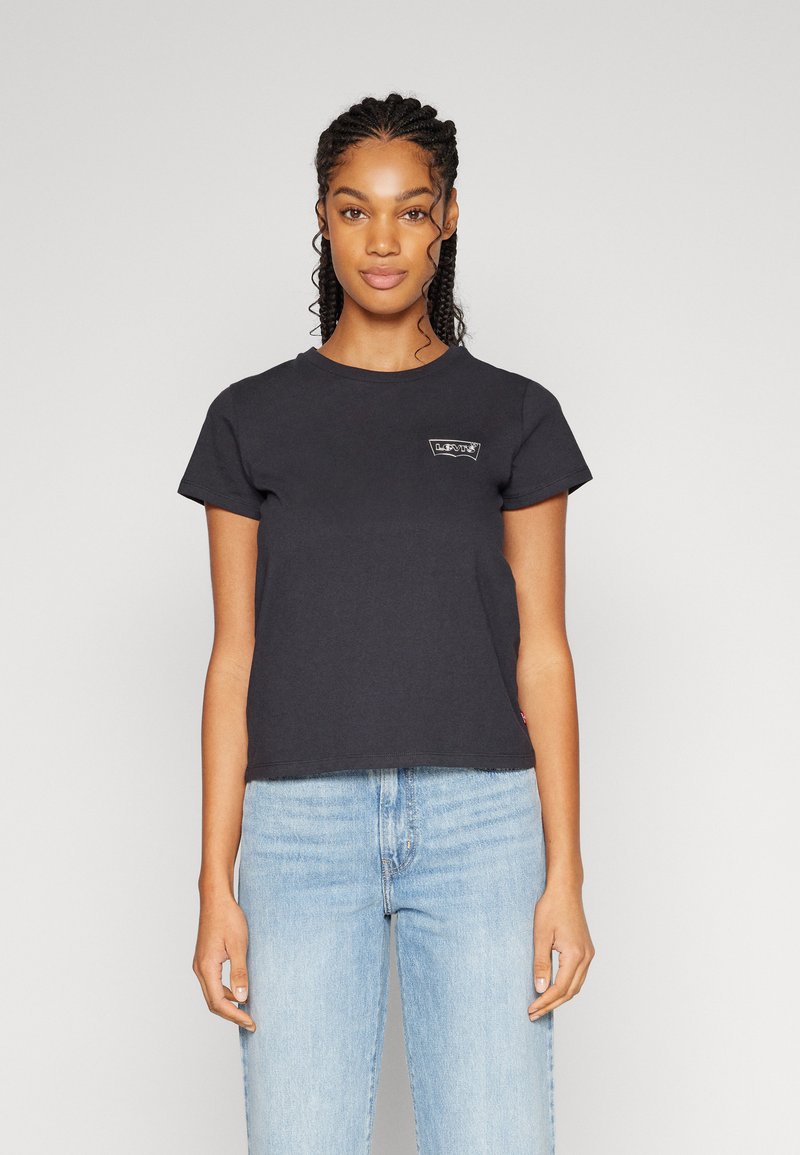 T-shirt noir en coton à manches courtes avec un col rond et un petit logo brodé sur la poitrine gauche, associé à un jean bleu clair.